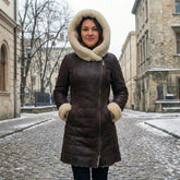 Woman wearing a long brown genuine leather shearling jacket with oversized cream fur hood in a snowy urban street