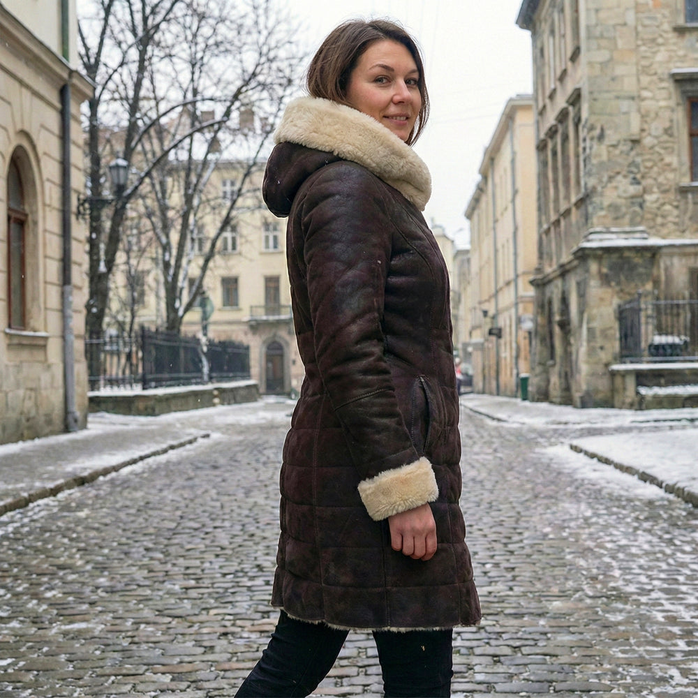 Side angle of a model wearing a slim-fit long-length winter leather coat highlighting the genuine cream shearling cuffs and structured silhouette.
